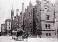 Two horses pull a streetcar in front of a four storey Gotchic building